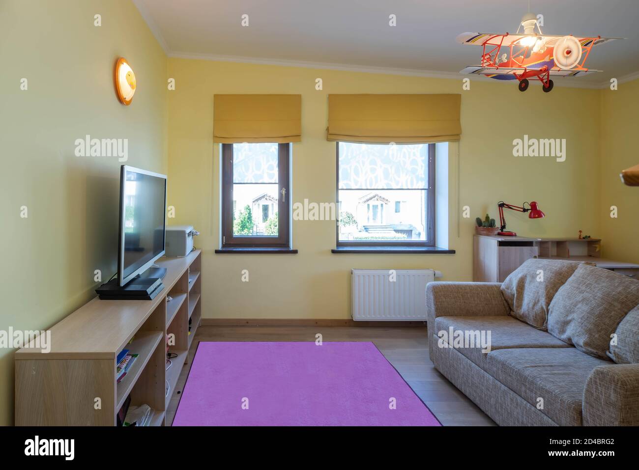 Modern interior of children`s room in luxury apartment. Cozy couch. TV on wooden shelf. Yellow walls. Stock Photo